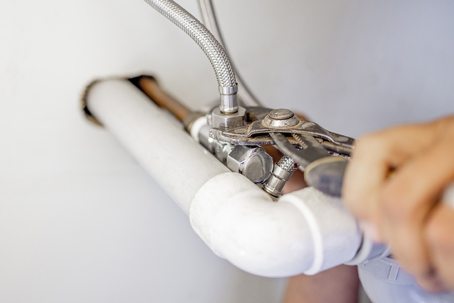 Person tightening pipe with a wrench.